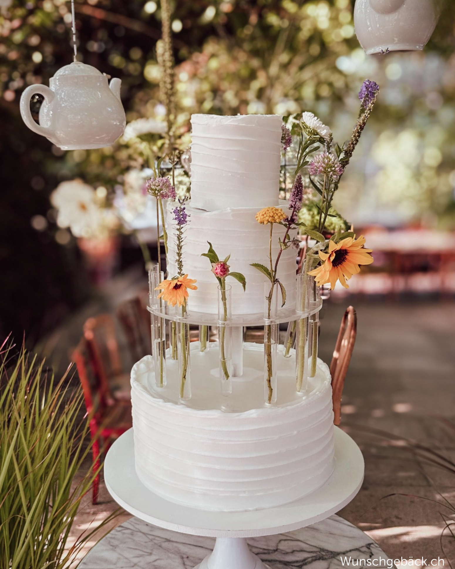 Outdoor wedding cake displayed with Prop Options Floral Tiara cake separator in a garden setting