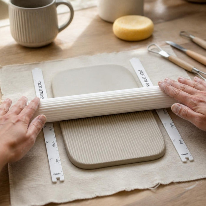 Clay thickness guides either side of a stoneware slab with a Prop Options reeded texture roller